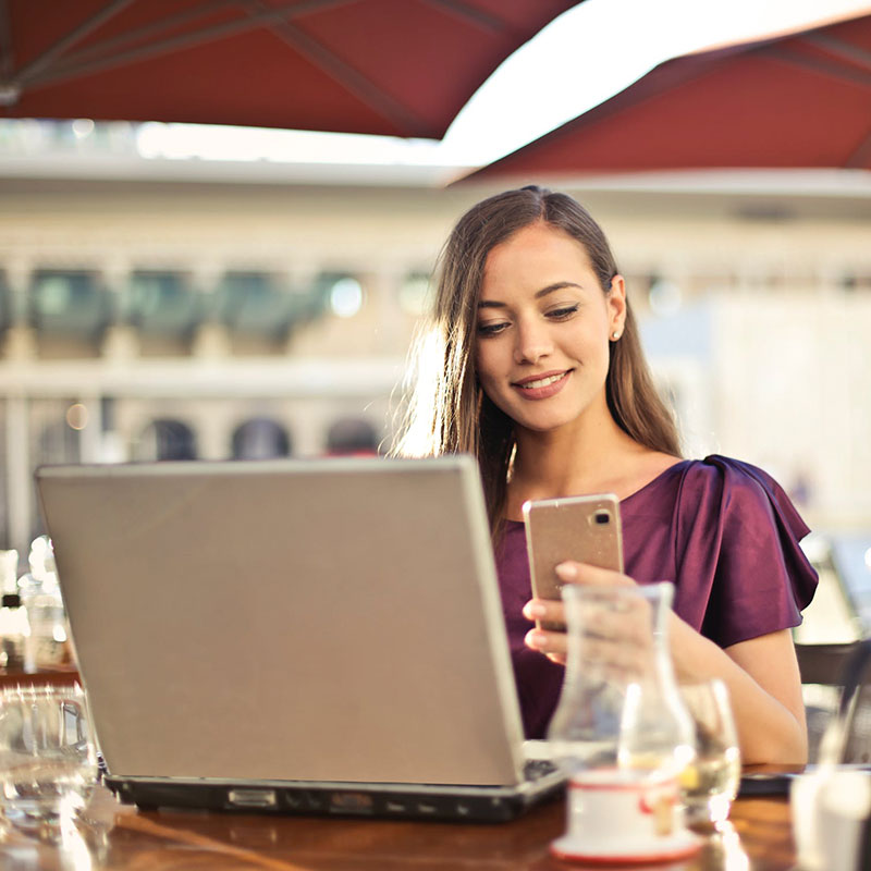 Women sitting at table in front of laptop holding smart phone