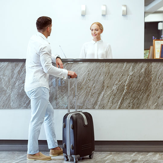 Man at reception desk of hotel with woman behind the desk smiling