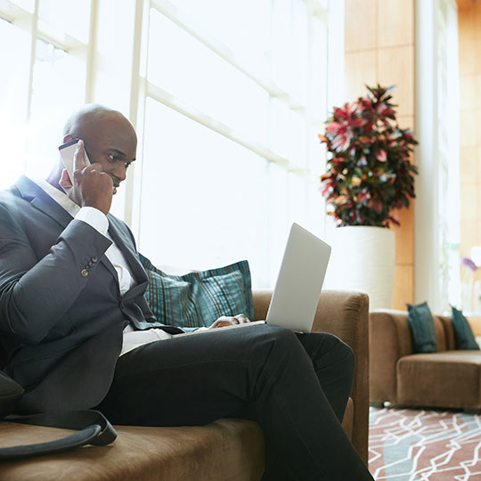 Man sitting and talking on phone with laptop on his legs