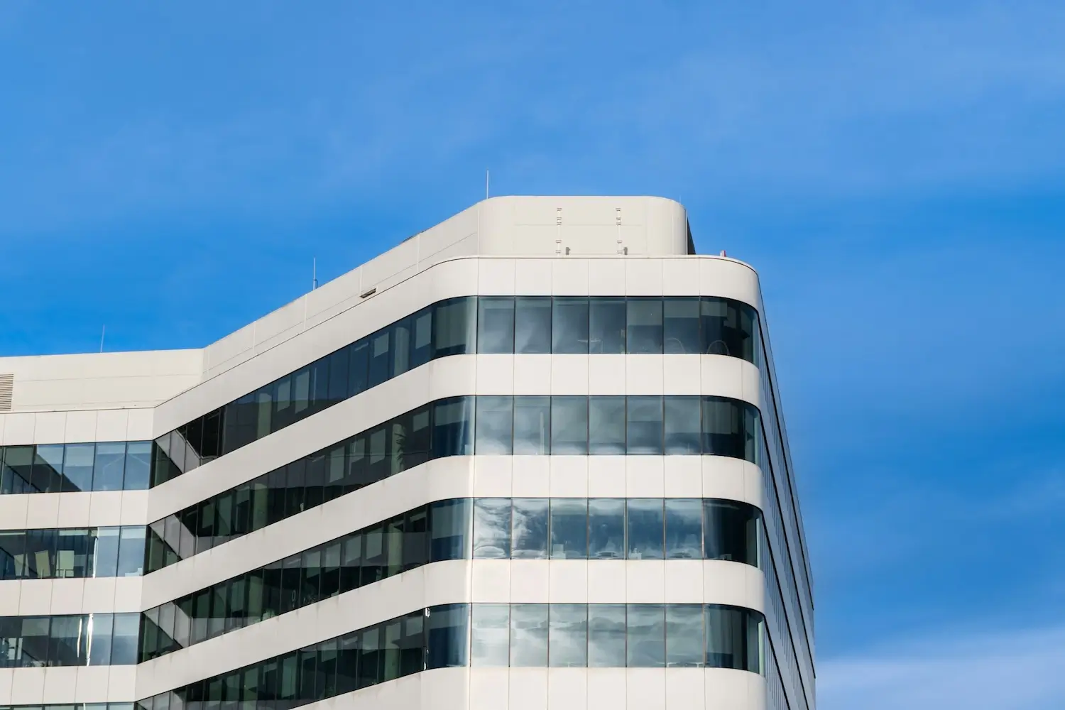 alternating concrete and windows on top floors of office building against blue sky with light reflected by windows